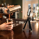 Bartender makes drink in front of phone camera on tripod atop the bar counter